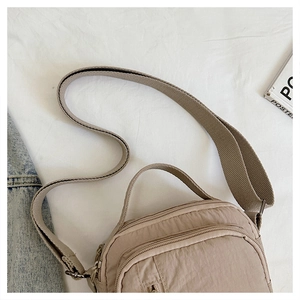 Close-up of light khaki nylon shoulder bag with multi-layer zippers and adjustable strap