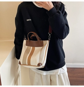 Detail of striped canvas tote bag with brown leather handles and adjustable shoulder strap