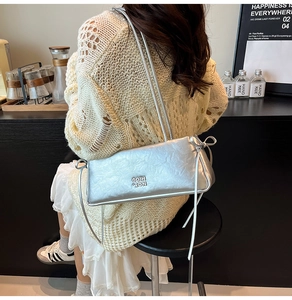 Sac à bandoulière argenté brillant avec nœud porté par un mannequin dans un café moderne
