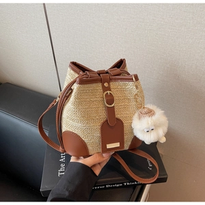 Detail of woven straw bucket bag with dark brown leather trim and plush sheep pendant
