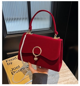 Detail of red velvet handbag featuring golden circular lock and pearl chain strap