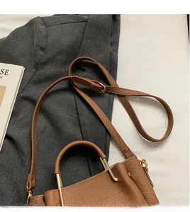 Detail of brown lychee leather shoulder bag with adjustable strap and gold metal handle