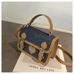 Detail view of denim crossbody bag with brown leather trim and heart fashion patch