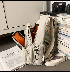 Detail view of beige nylon mini backpack with vibrant orange lining and side drawstring pocket