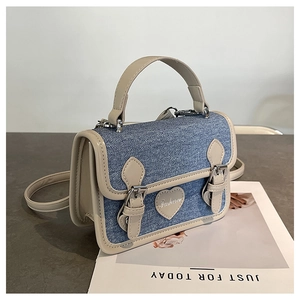 Detailed close-up of a blue denim mini bag featuring heart patch and leather trim