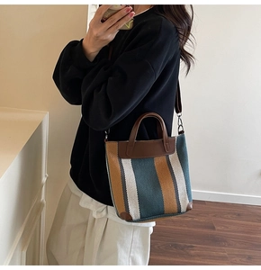 Detail of a woven canvas bucket bag with brown leather handles and striped texture