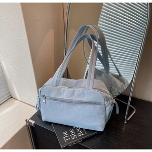 Detailed view of light blue padded nylon tote bag with silver zipper on a black book