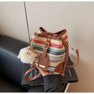Close-up of woven bucket bag with striped pattern, leather strap and plush monster charm