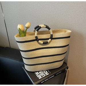Detail of hand-woven straw tote with black stripes, round handles, and tulip floral accents