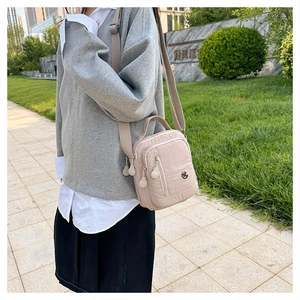 Detail of a beige nylon crossbody bag with multiple zip pockets and round pulls on the lawn