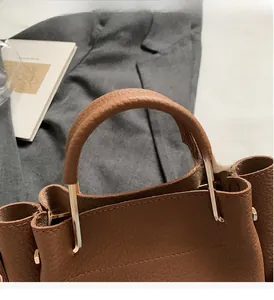 Close-up of brown litchi leather texture and golden handle bracket of bucket bag