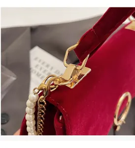 Detail of red velvet handbag with golden hardware, pearl chain, and luxury texture
