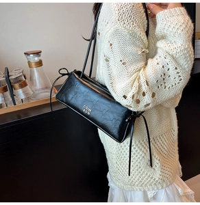 Détail du sac à bandoulière en cuir noir avec logo argenté et cordon de serrage noeud