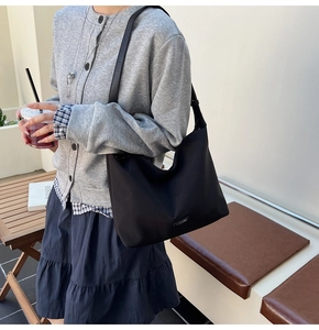 Black nylon hobo bucket bag with metallic logo detail worn by a model in an urban setting