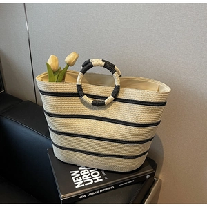 Detail of hand-woven straw tote bag with black stripes and decorative circular handles