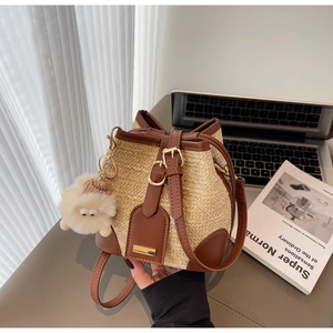 Detail of woven straw bucket bag with brown leather trim and cute sheep charm pendant
