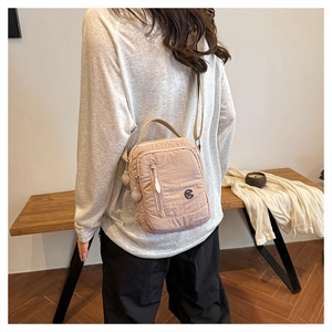 Side view of lightweight nylon crossbody bag in beige-pink worn by a model