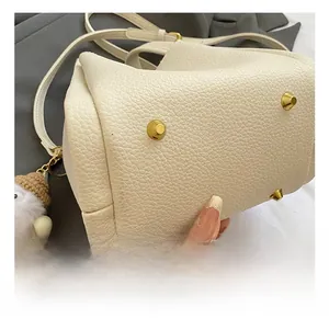Detail of white lychee leather bag base with four golden metal feet and plush charm