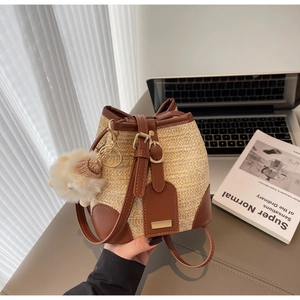 Detail of straw woven bucket bag with brown leather trim and cute white lamb pendant