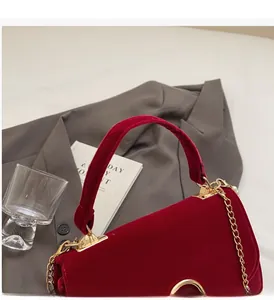 Detail of red velvet handbag showing golden metal chain strap and elegant clasp closure