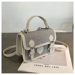 Detailed shot of a stylish denim square bag featuring heart emblem and twin buckles