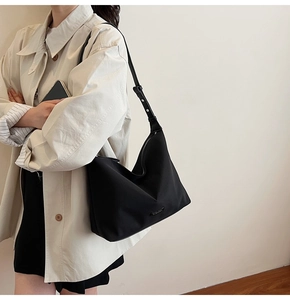 Detail of minimalist black hobo bag with adjustable strap and metal logo on a model
