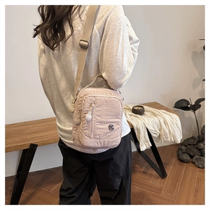 Close-up of pink nylon crossbody bag with adjustable wide strap and round metal logo