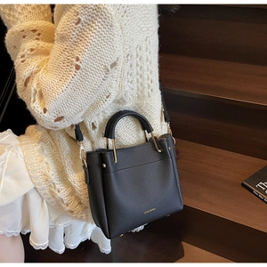 Close-up of a black lychee-textured bucket bag with golden hardware on wooden steps