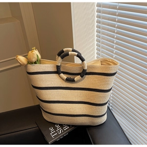 Close-up of beige woven straw tote bag with black stripes and circular resin handles