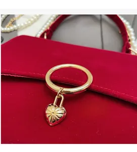 Detail of red velvet handbag with golden heart padlock and elegant pearl handle accents