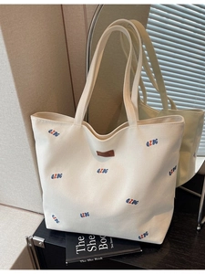 Minimalist beige canvas tote bag with embroidered letters and brown leather label