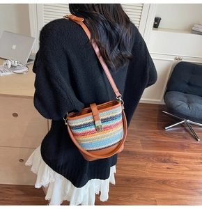 Detail of colorful woven straw bucket bag with brown leather strap worn crossbody