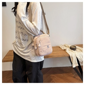 Detail view of pink wrinkled nylon crossbody bag with multiple zip pockets and beige strap
