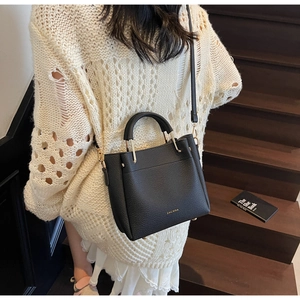 Detail of black pebbled leather bucket bag with gold hardware on a wooden staircase