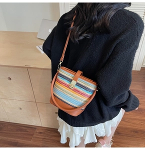 Detailed view of colorful woven straw bucket bag with brown leather trim and metal clasp