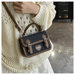 Close-up of denim crossbody bag with brown leather trim and heart fashion patch detail