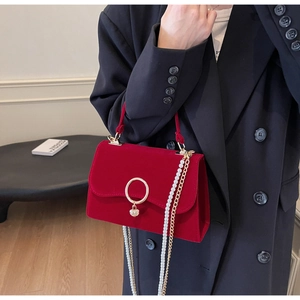 Detail of red velvet handbag with gold heart pendant and pearl chain strap on black suit