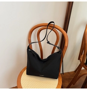 Close-up of a black minimalist nylon hobo bag on a wooden chair in a warm lifestyle scene