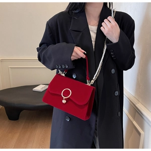 Detail of red velvet crossbody bag with gold hardware and pearl chain strap on model