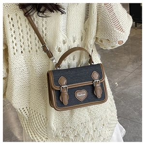 Detail of denim crossbody bag with brown leather trim and fashion heart patch