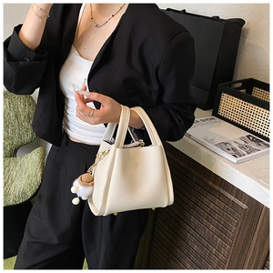 Detail of off-white lychee texture tote bag featuring a creative charm and metal feet