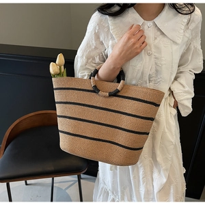 Close-up of a large straw tote bag with black stripes and unique circular woven handles