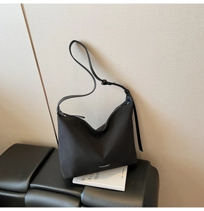 Detail view of a black nylon tote bag on a black bench with an adjustable shoulder strap