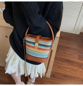 Detail of colorful woven straw bucket bag with brown leather trim and gold buckle lock