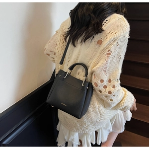 Detail showing the black lychee pattern leather and gold metal handle of the shoulder bag