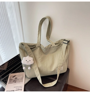Gros plan du grand sac de voyage vert clair avec breloque nuage en peluche et bandoulière