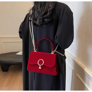 Detail of red velvet handbag with gold ring clasp and pearl chain strap on model