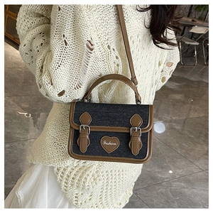 Detail of vintage denim crossbody bag with brown leather trim and heart fashion patch