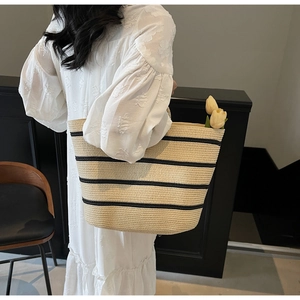 Large woven straw tote bag with black stripes carried by model in white dress