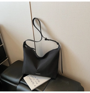 Close-up of black nylon hobo bag with silver logo plaque on a leather stool and book